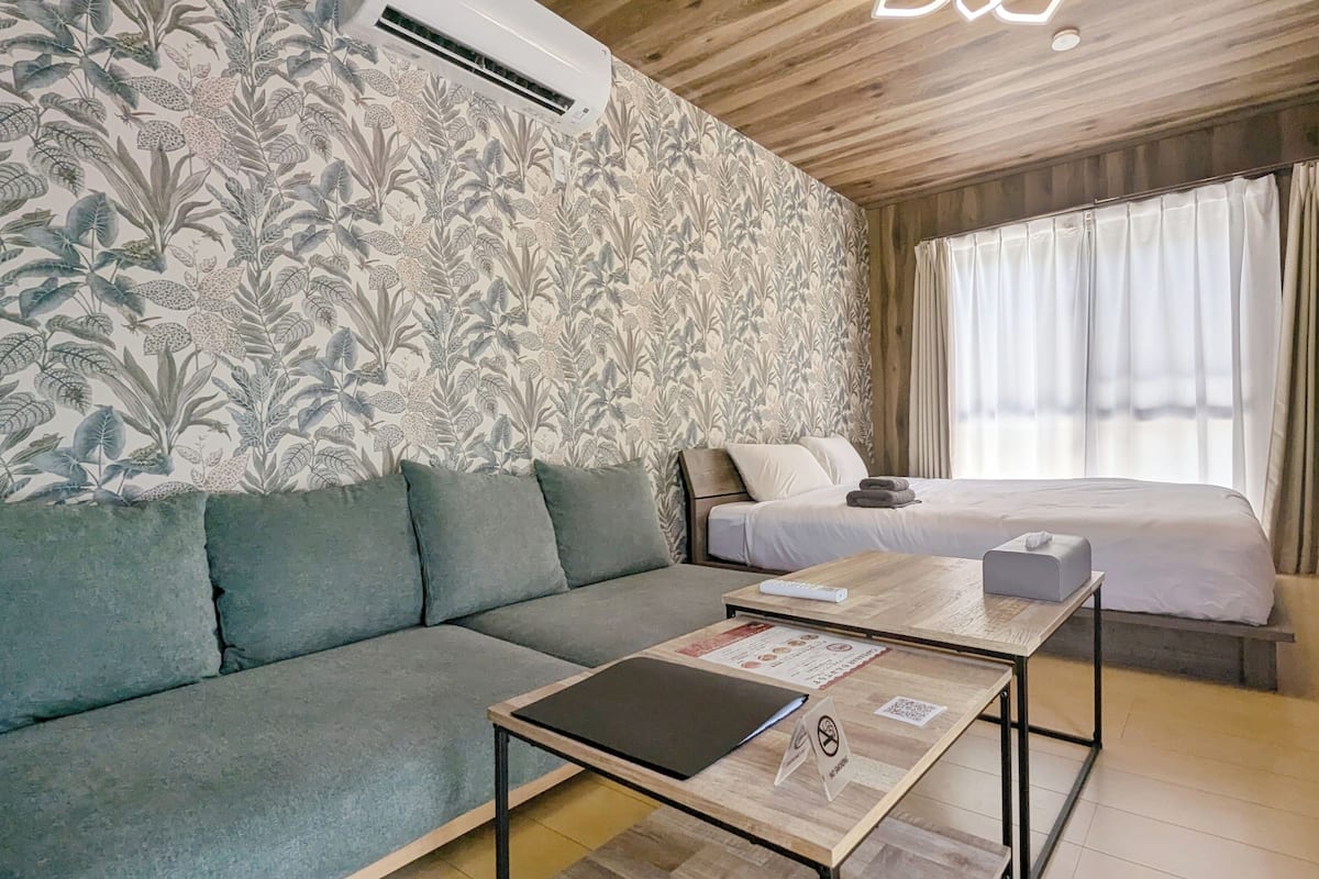 Ein Zimmer mit einem Bett, einem Schlafsofa, einem Tisch und einer Wand mit einem Blumenmuster.