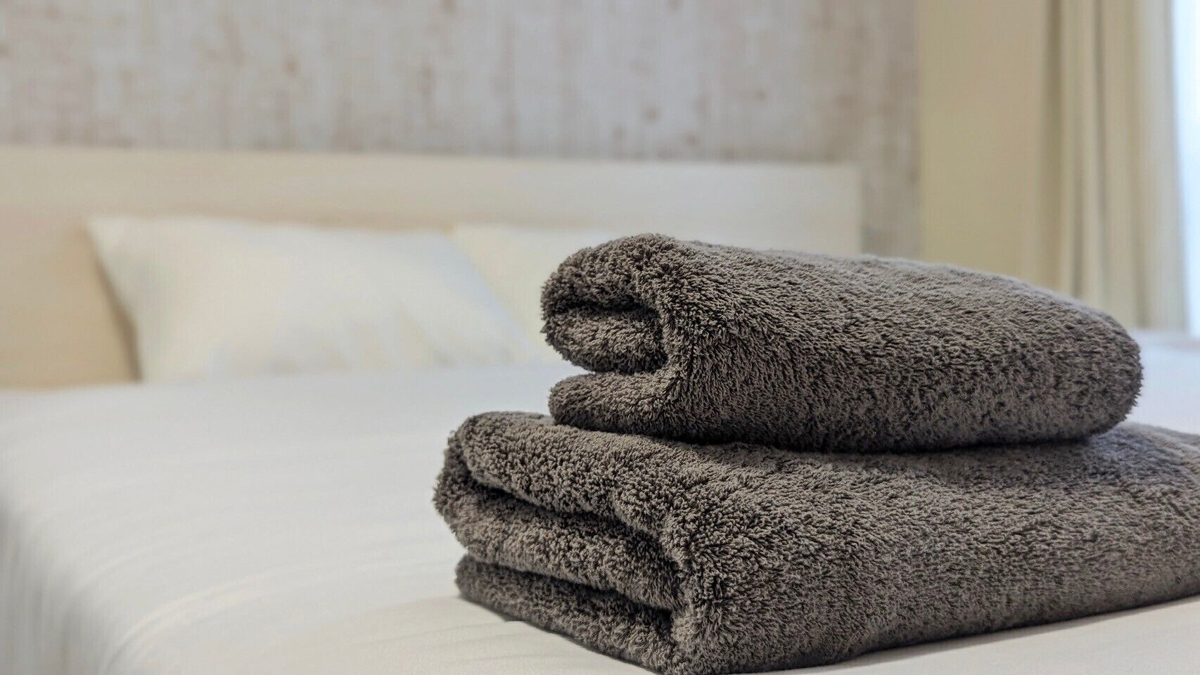 Cama bem arrumada com um cobertor cinza dobrado e um travesseiro.