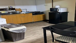A compact kitchen with wooden cabinets, a microwave, a small refrigerator, and a trash bin. - Minpaku Ota Building 3 (Otaru)