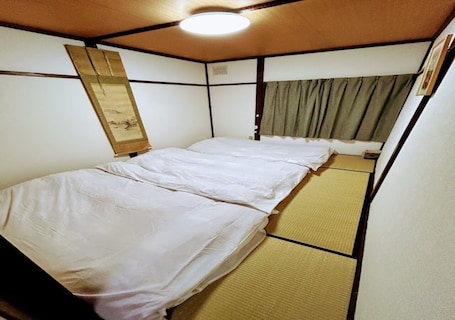 A small, single-bed room with a tatami mat floor and a traditional Japanese shoji screen.