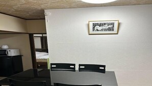 A small dining area with a table and chairs, a framed picture on the wall, and a microwave on a cabinet. - Minpaku Ota Building 3 (Otaru)