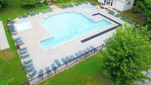 A rectangular swimming pool with a surrounding deck and lounge chairs, a small building with a red roof, and a larger building with a tiled roof.