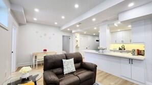 A modern kitchen with white cabinets, a dining area with a table and chairs, and a leather sofa with a patterned pillow. - Serene High-celling Retreat in Upsacle and Safe Neighbourhood (Oakville)