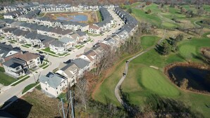 An aerial view of a residential area with houses arranged in a circular pattern around a central green space, including a pond and a golf course. - Serene High-celling Retreat in Upsacle and Safe Neighbourhood (Oakville)