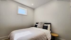 A bedroom with a bed, a bedside table, a window, and a wall-mounted light. - Serene High-celling Retreat in Upsacle and Safe Neighbourhood (Oakville)