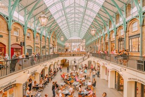 Un mercado interior amplio con un techo de vidrio alto y varios niveles de tiendas y zonas de estar.