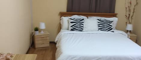 A bedroom with a bed, a nightstand, a lamp, a wall-mounted air conditioner, and a painting.