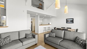A modern living room with two grey sofas, a dining table, and a kitchen in the background. - Lakeside Landing - lakefront and walk to town (Queenstown)