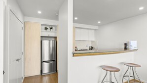 A modern kitchen with a stainless steel refrigerator, wooden cabinets, and a wooden countertop. There are two bar stools and a small shelf with plants. - Lakeside Landing - lakefront and walk to town (Queenstown)
