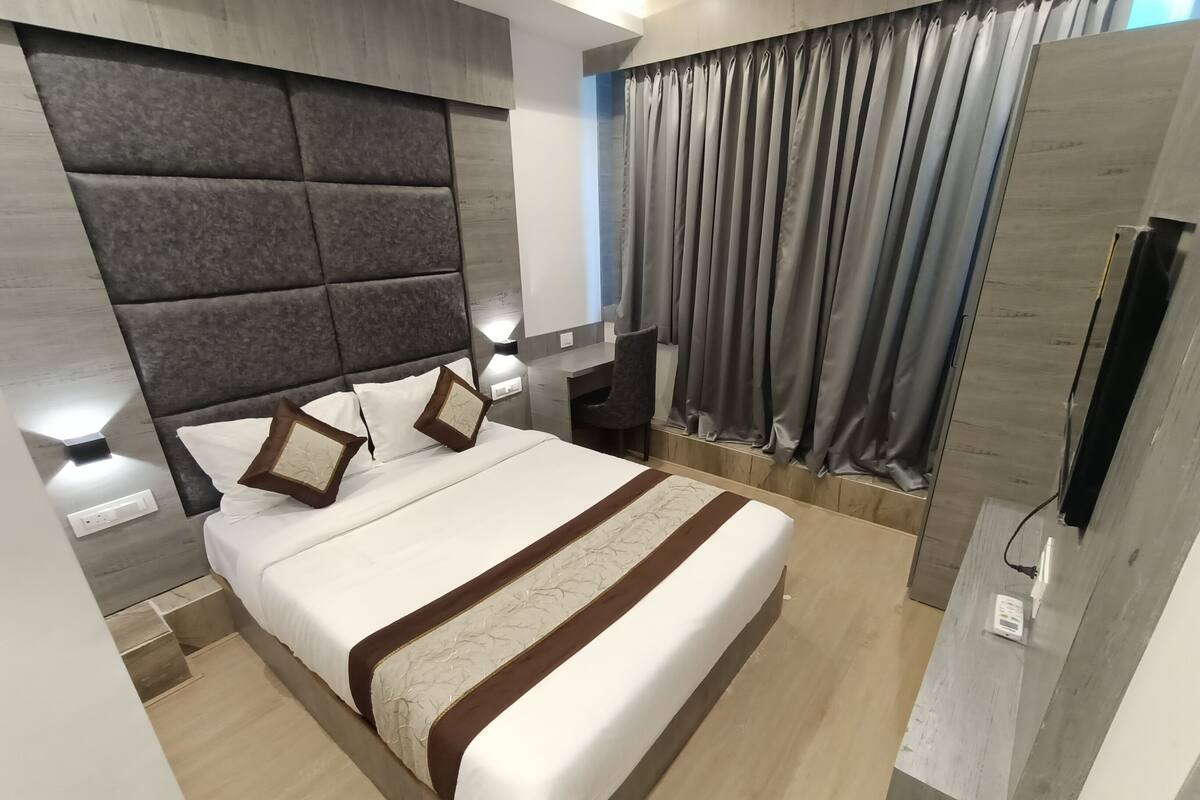 Une chambre d’hôtel moderne avec un grand lit, une tête de lit au motif texturé, une table de chevet avec une lampe et une grande fenêtre avec des rideaux.