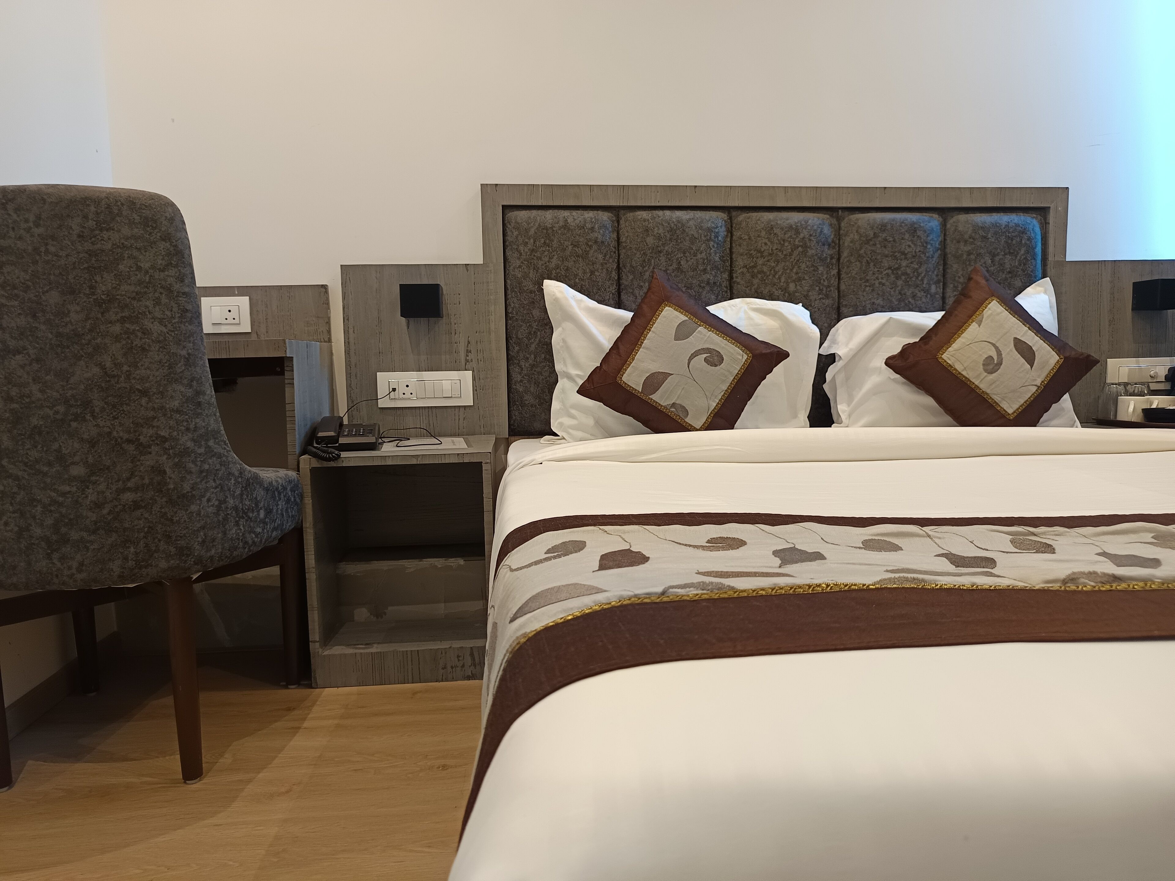 A hotel room with a bed, a chair, a nightstand, and a wall-mounted TV.