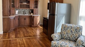 A kitchen with wooden cabinets, a stainless steel refrigerator, and a patterned armchair. - BigWave 1 -Total reno 1st fl, near ASV & Colleges (Oneonta)