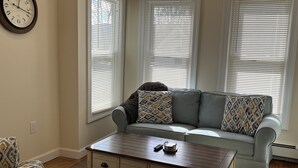 A living room with a sofa, a coffee table, and a clock on the wall. - BigWave 1 -Total reno 1st fl, near ASV & Colleges (Oneonta)