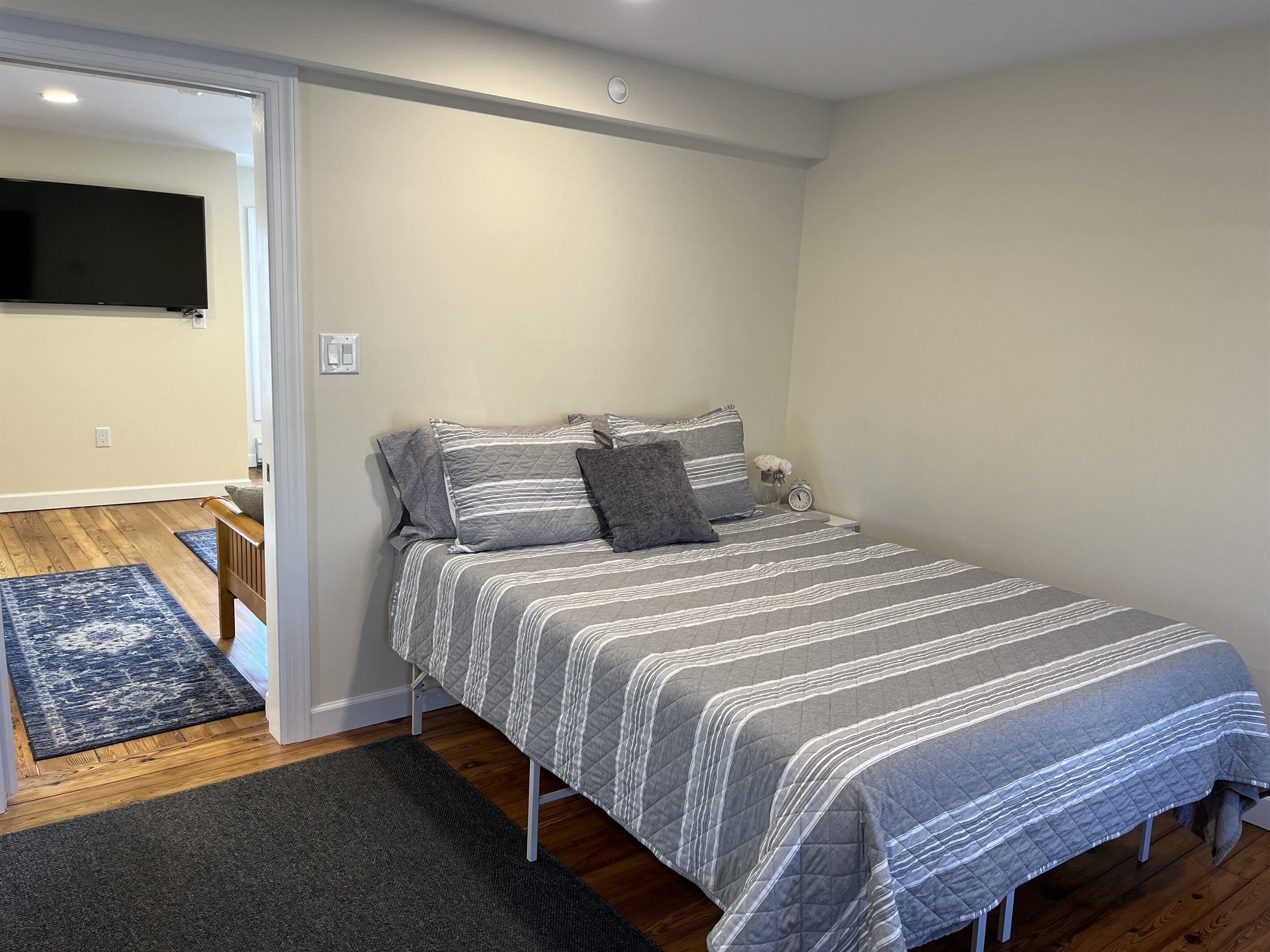 Une chambre à coucher comprenant un lit, une table de chevet, un téléviseur fixé au mur et une porte donnant sur une autre pièce.