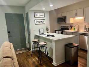 A modern kitchen with a central island, bar stools, a microwave, and a dishwasher.