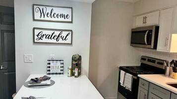 A kitchen with a white countertop, a microwave, cabinets, and a sign that reads "Welcome Grateful".