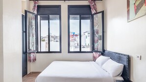 A bedroom with a bed, two windows with curtains, a nightstand, and a wall-mounted light switch. - Hôtel Mauritania Centre Tangier (Tangier)