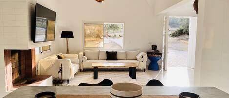 A modern living room with a fireplace, a sofa, a coffee table, and a dining area with a rug and bowls.