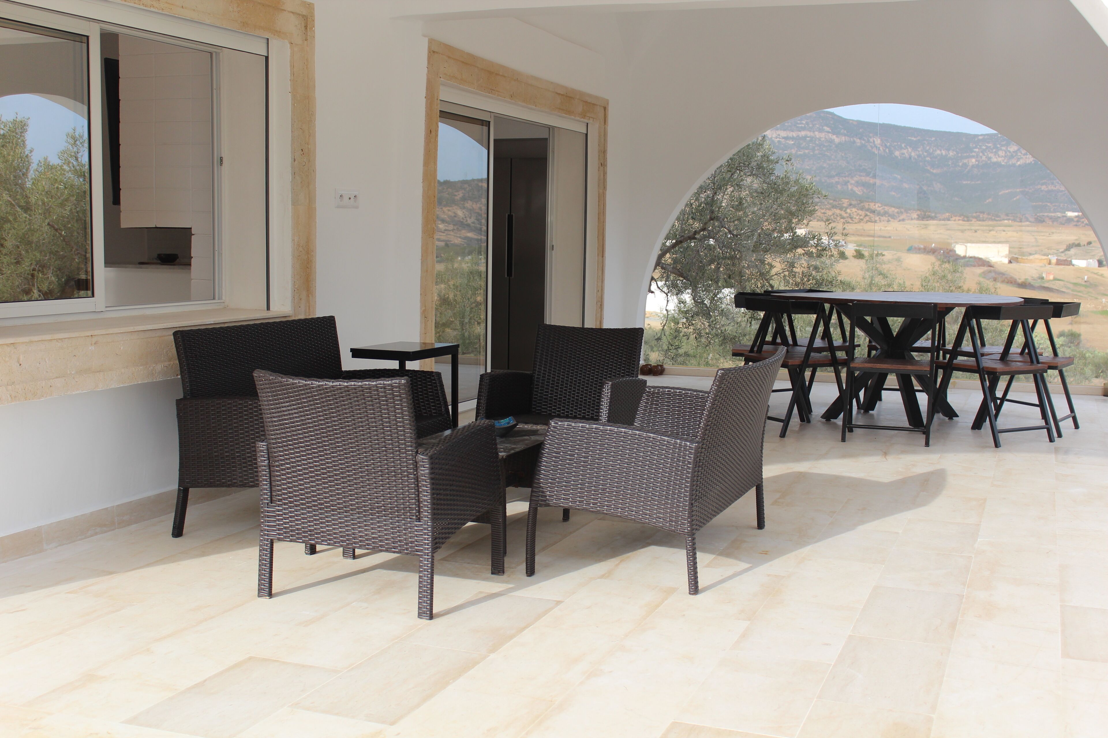 An outdoor patio with wicker furniture, a dining table, and a view of the countryside.