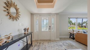 Un pasillo con un espejo decorativo, una consola con detalles naturales, un tapete estampado y vistas al exterior a través de una ventana.