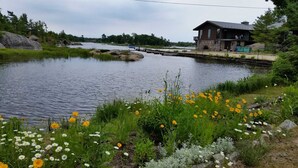 Un chalet au bord de la rivière, doté d’un quai, entouré d’une végétation luxuriante et d’une grande variété de fleurs sauvages.