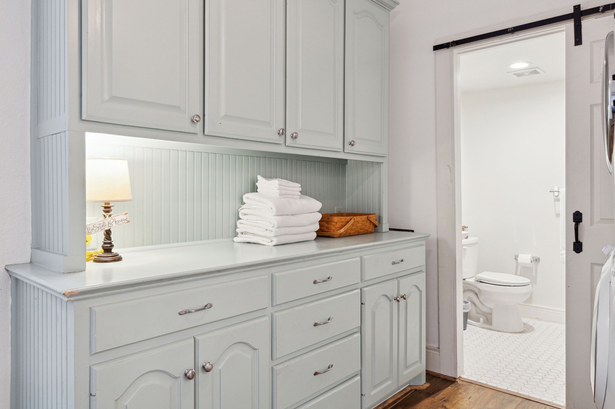 Une salle de bain avec un meuble-lavabo blanc, une pile de serviettes et un panier.