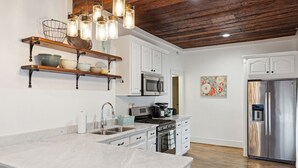 A modern kitchen with white cabinetry, a marble countertop, a stainless steel refrigerator, and a wooden ceiling. - Birdsong Retreat in McKinney (McKinney)