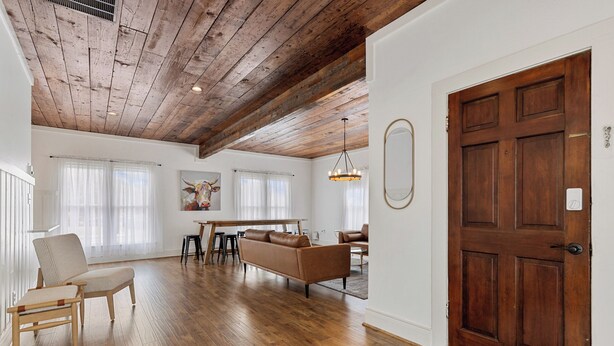 A spacious living room with a wooden ceiling, a brown leather sofa, and a dining area with a wooden table and chairs. - Birdsong Retreat in McKinney (McKinney)