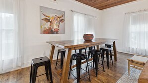 A dining area with a wooden table, black bar stools, and a cow painting on the wall. - Birdsong Retreat in McKinney (McKinney)