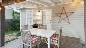 A covered patio with a white table and chairs, a star decoration on the wall, and string lights. - Birdsong Retreat in McKinney (McKinney)