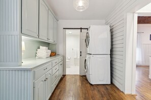 A laundry area with a washing machine and dryer, wooden flooring, and light blue cabinetry. - Birdsong Retreat - Historic + Modern + Walk to DT (McKinney)