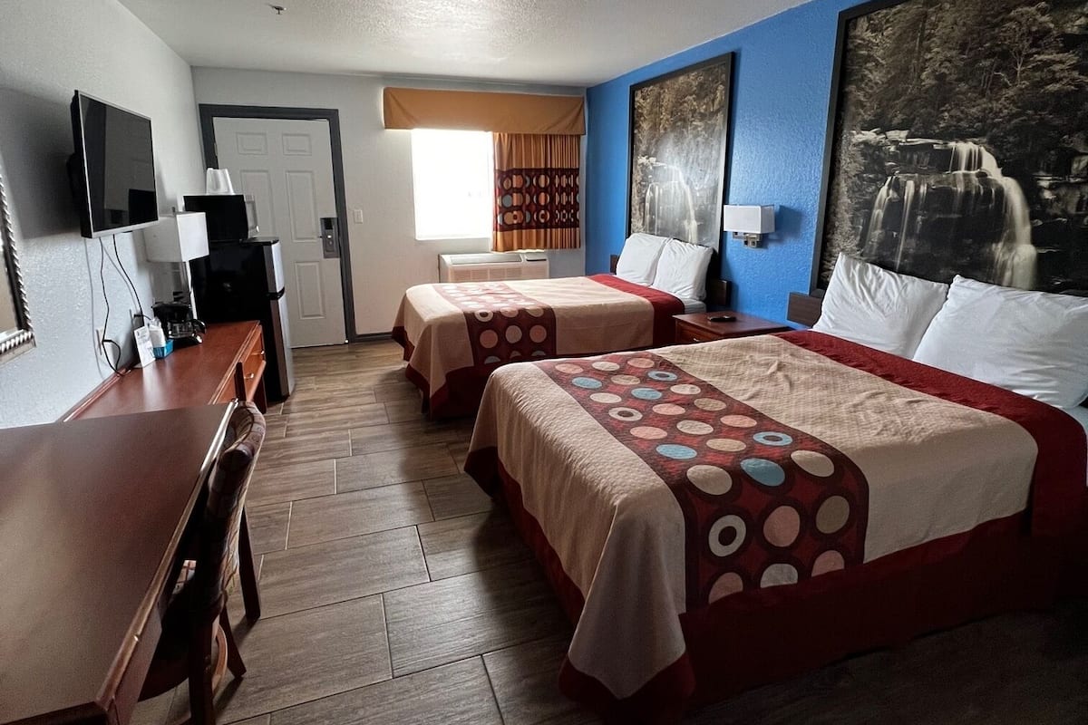A hotel room with two beds, a desk, a coffee machine, and a large window.