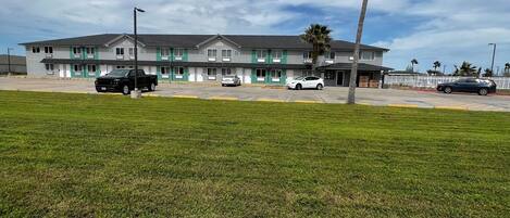 A motel with a parking lot, a grassy field, and a palm tree.