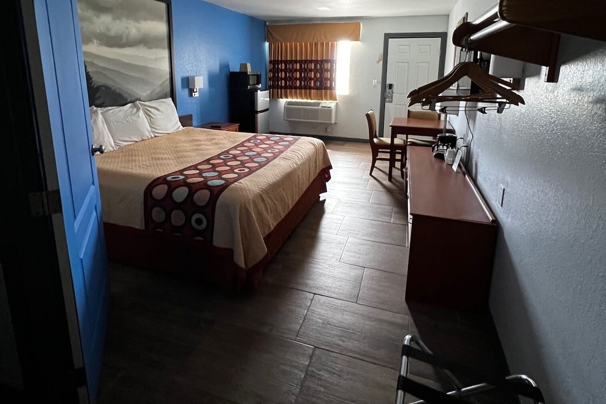 A bedroom with a bed, a desk, and a chair. There is a window with curtains and a door.