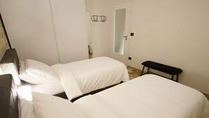 A bedroom with two beds, a bench, a mirror, and a hanging light fixture. - Venezia a 15 min bus sotto casa ogni 10 min, parcheggio libero, animali ammessi. (Chirignago-Zelarino)