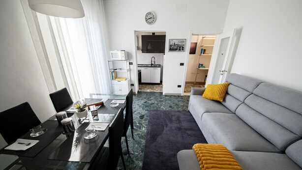 A modern living room with a grey sofa, a dining table set for two, and a kitchen in the background. - Venezia a 15 min bus sotto casa ogni 10 min, parcheggio libero, animali ammessi. (Chirignago-Zelarino)