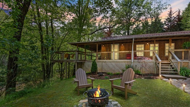 A cabin with a fire pit, two Adirondack chairs, and a deck.