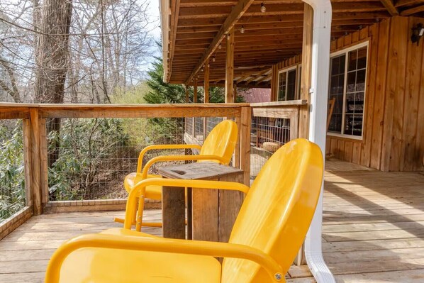 Una terraza de madera con sillas amarillas y una mesa, rodeada por una valla de madera y árboles.