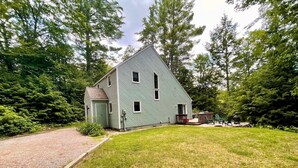 Une maison à deux étages, avec une façade verte, un porche à l’avant et un petit garage attenant.