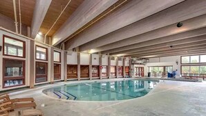 Une grande piscine intérieure dotée de chaises longues en bois, de hauts plafonds et de grandes fenêtres.