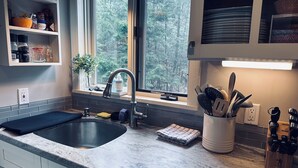 Une cuisine équipée d’un évier, d’une fenêtre et d’un plan de travail sur lequel sont disposés divers ustensiles de cuisine.
