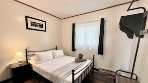 Una habitación pequeña y limpia con una cama individual, una mesita de noche con lámpara, un cuadro en la pared y una ventana con cortinas.