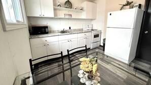 Una cocina moderna con armarios blancos, microondas, estufa y refrigerador. Hay una mesa de comedor de vidrio con sillas y un jarrón con flores.