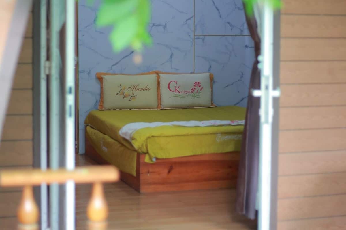A small, cozy room with a bed, two pillows, and a wooden floor.
