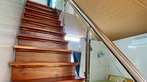 A wooden staircase with a glass railing leading to a room with a bed and a nightstand. -  Homestay Tuyet Anh (Tri Ton)