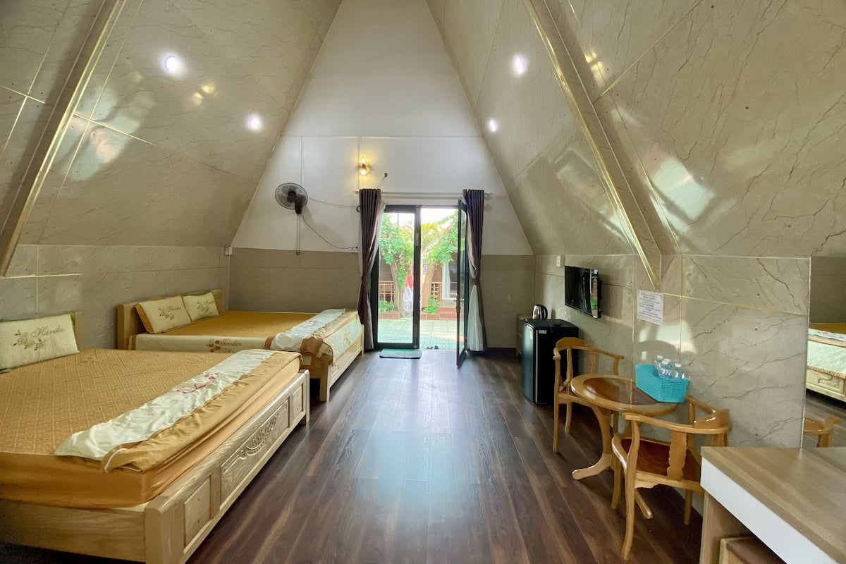 A triangular room with two beds, a wooden table, a TV, and a ceiling fan.