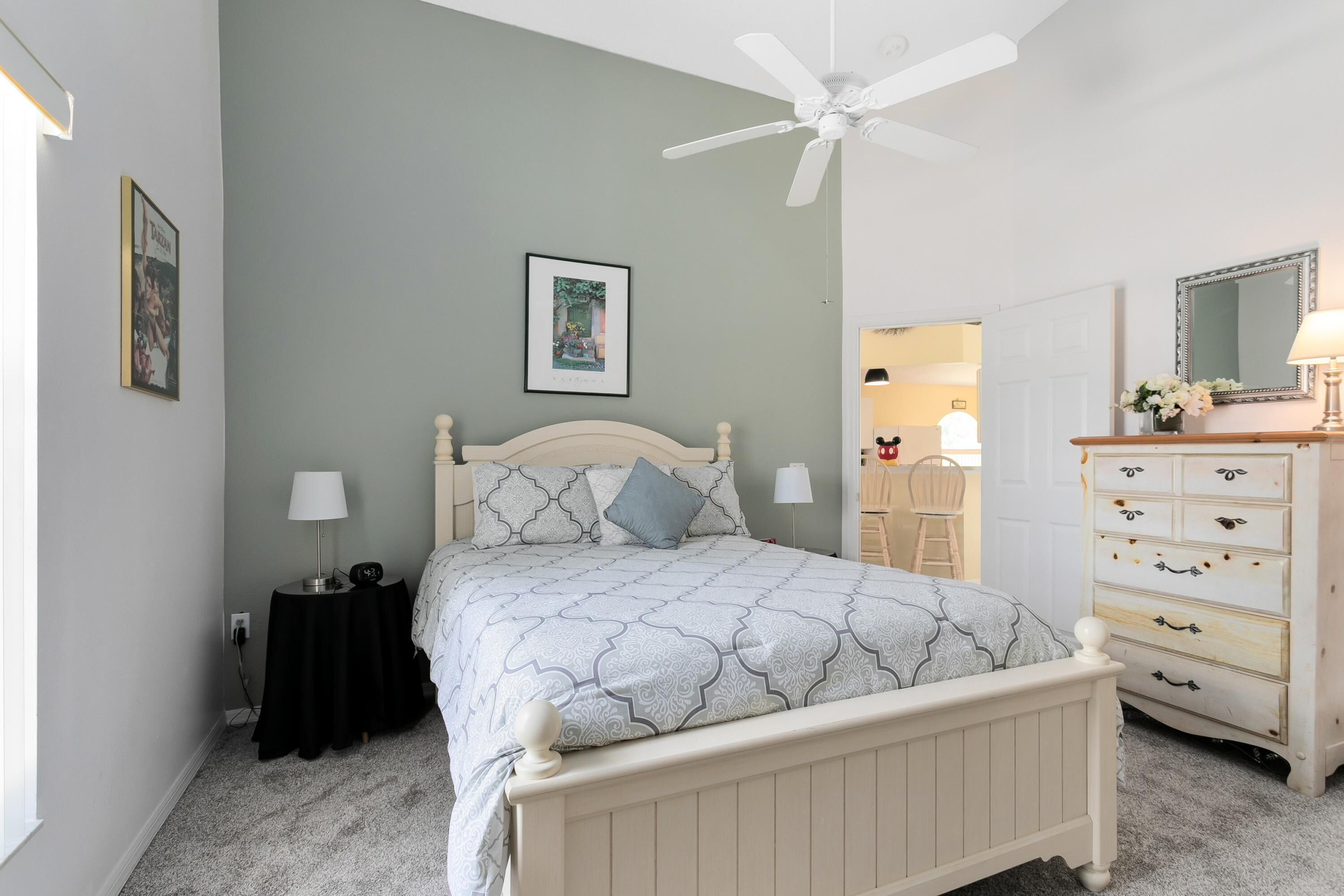 A bedroom with a bed, a dresser, a ceiling fan, and a framed picture on the wall.