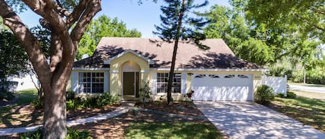 A single-story house with a garage, a front yard with a tree, and a clear sky.