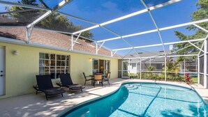 A covered swimming pool with lounge chairs and a table, surrounded by a glass enclosure. - 3 Bedroom 2 Bathroom Disney Vacation Home (Davenport)