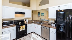A modern kitchen with white cabinets, a black refrigerator, a coffee maker, and a dishwasher. - 3 Bedroom 2 Bathroom Disney Vacation Home (Davenport)